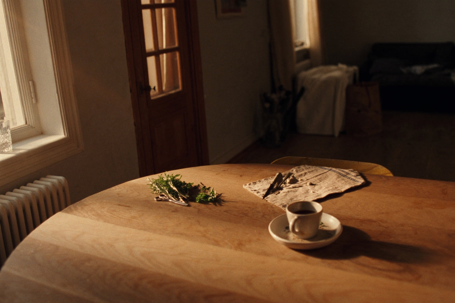 A wooden table with morning coffee, linen and freshly cut herbs in golden light